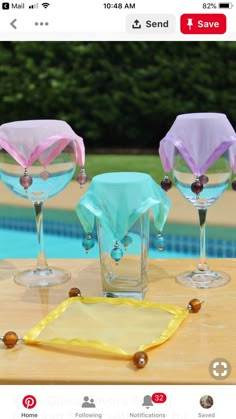 three empty wine glasses sitting on top of a wooden table next to a swimming pool