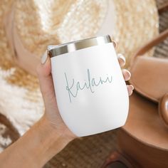 a person holding a white cup with the word kalakau written on it in cursive writing