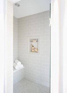 a white tiled bathroom with a shower stall and toilet paper roll holders on the wall