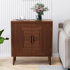 a wooden cabinet sitting next to a couch in a living room with white walls and wood flooring