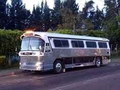 an old silver bus is parked on the side of the road in front of some trees