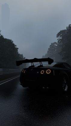 a black sports car driving down a wet road in the rain with its lights on