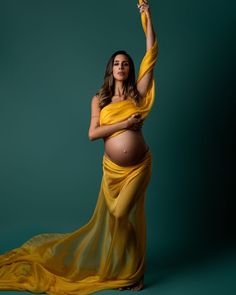 a pregnant woman in a yellow dress is posing for a photo with her hands up