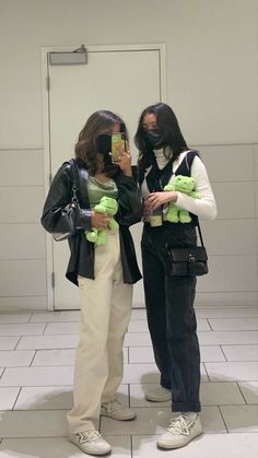 two young women standing next to each other holding cell phones and stuffed animals in their hands