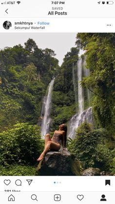 a woman sitting on top of a rock in front of a waterfall with lots of greenery