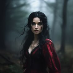 a woman with long black hair standing in the woods wearing a red dress and looking at the camera