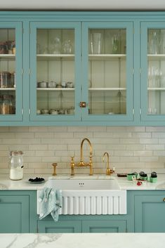 a kitchen with blue cabinets and white marble counter tops, gold faucets and brass fixtures