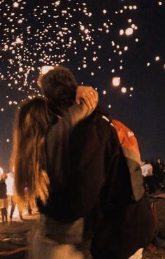 two people standing next to each other with fireworks in the sky