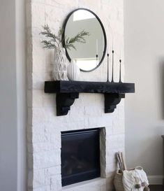 a fireplace with candles and a mirror on it's mantle, in front of a white brick wall