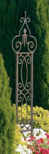 a tall metal plant stand sitting in the middle of a flower filled garden with lots of red and white flowers