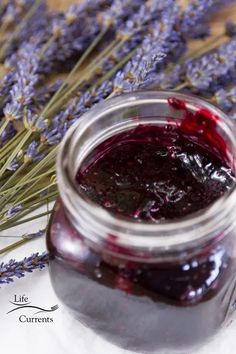 a jar filled with blueberry jam sitting on top of a table next to lavender flowers