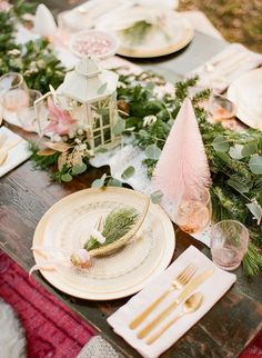 the table is set with plates, silverware and greenery