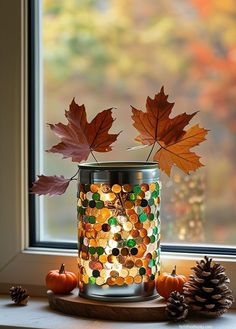 a glass jar filled with lots of different colored beads and leaves sitting on top of a window sill