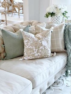 a couch with many pillows on it in front of a vase filled with white flowers