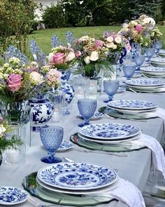 a table set with blue and white plates and vases filled with flowers on it