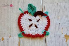 a crocheted apple with a green leaf on it sitting on a wooden surface