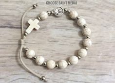 Saint medal rosary bracelet is made with 8mm white faux howlite beads and cross,silver tone spacer beads,cross and 1cm silver tone saint medal of your choice. For Men and Women . Adjustable cording ,fits a wrist size from 6.5 x7.5 inches. Metal parts made in Italy. Hand made in Medjugorje. A nice gift for a loved one or a statement of faith to wear yourself. For more similar items and different colors visit our store: https://www.etsy.com/shop/Thelightjewelry?ref=seller-platform-mcn Adjustable Miraculous Medal For Gift, Adjustable Silver Rosary Bracelet With Miraculous Medal, Adjustable Silver Spiritual Jewelry And Charms, Adjustable Silver Cross Beaded Bracelets, Adjustable Silver Beaded Bracelets With Cross Shape, Adjustable Silver Beaded Cross Bracelets, Nickel Free Cross Bracelet With Spiritual Style, Nickel-free Cross Bracelet For Spiritual Style, Adjustable Spiritual Rosary