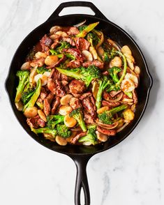 a skillet filled with stir fry vegetables on top of a white countertop next to a wooden spoon