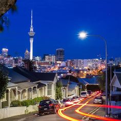 the city skyline is lit up at night with cars driving down the street in front of it