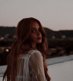 a woman with long red hair standing on a roof