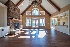 a large open living room with wood floors and vaulted ceiling, stone fireplace in the center