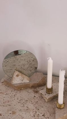 two white candles sitting on top of a table next to a mirror and candle holder