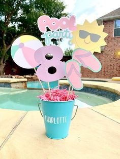 a blue bucket filled with pink and yellow cupcakes next to a swimming pool