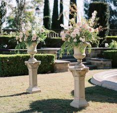 two vases with flowers are sitting in the grass near some bushes and water fountain