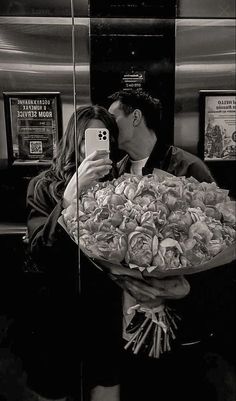 a man holding a bouquet of flowers taking a selfie with his cell phone in front of him