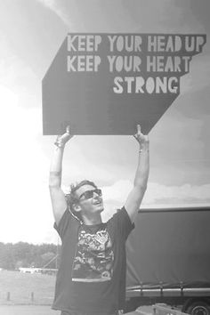 a man holding up a sign that says keep your head up keep your heart strong