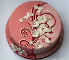 a pink cake with white flowers and swirls on the top is sitting on a plate