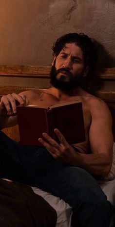 a shirtless man reading a book while laying in bed