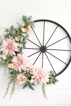 a bicycle wheel decorated with flowers and greenery on the side of a white wall