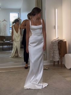 a woman standing in front of a mirror wearing a white dress