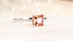 This beautiful ring features a princess cut, square shape, sunrise genuine topaz. The alluring gemstone is set on a minimalist four prong mount with a dainty band of minimalist elegance. Topaz is the traditional November birthstone. The preferred varieties of topaz hues for November include yellow, orange, pink, violet, brown and, very rarely, red but topaz also comes in colorless, light blue and teal shades. Dimensions -6mm square, princess-cut  -Band: 1.8mm -Stone mount from band to top: 6.5mm (above the finger) Saturation: medium-saturated Tone: sunrise yellowish orange  Hardness: 8 on the Mohs Hardness Scale, a durable gem, suitable for daily wear. Custom Option:  - 6mm, square-shape light blue natural topaz or any other colored gemstone. Origin: Natural, color enhanced Teal Shades, Violet Brown, Yellow Orange Pink, Mystic Topaz Ring, Dainty Band, November Birthstone, Mystic Topaz, Topaz Ring, A Princess