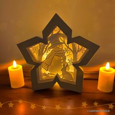 an origami snowflake with three lit candles on the table next to it