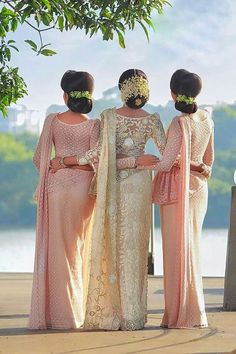 three women standing next to each other in front of a body of water with trees