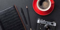 an old camera, pen, pencils and cup of coffee on a black table