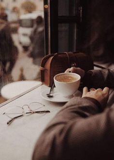 a person sitting at a table with a cup of coffee and reading glasses on it