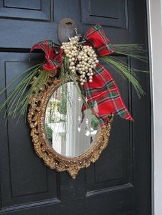 a wreath with berries and pine cones hanging from the front door, decorated with a red plaid bow