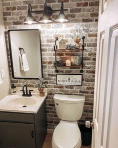 a white toilet sitting next to a sink in a bathroom under two lights on a brick wall