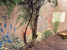 a wall painted with flowers and plants next to a tree