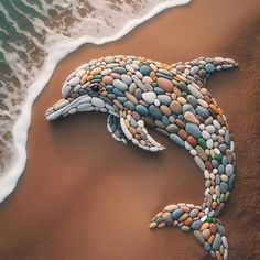 a sea turtle made out of rocks on the sand next to the ocean water and waves