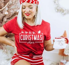 a woman with white hair wearing a red and white christmas t - shirt sitting in front of a christmas tree