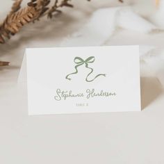 a white card with a green bow on it next to some pine cones and leaves