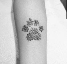 a small black and white flower tattoo on the left inner arm, with three flowers around it