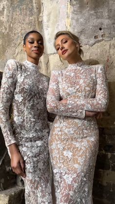 two women standing next to each other wearing dresses with long sleeves and sheer laces