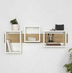 three white shelves with books, plants and other items on them against a white wall