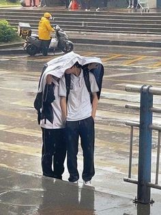 two people standing in the rain with an umbrella over their heads and one person covering his face