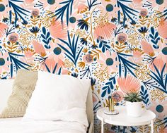 a white bed sitting next to a wall covered in pink and blue floral wallpaper